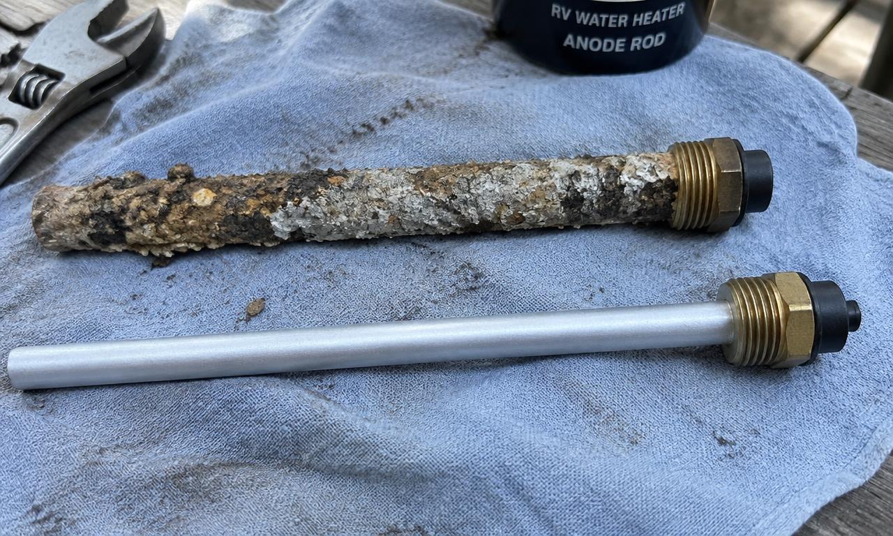 Corroded RV water heater anode rod beside a new one on a shop towel